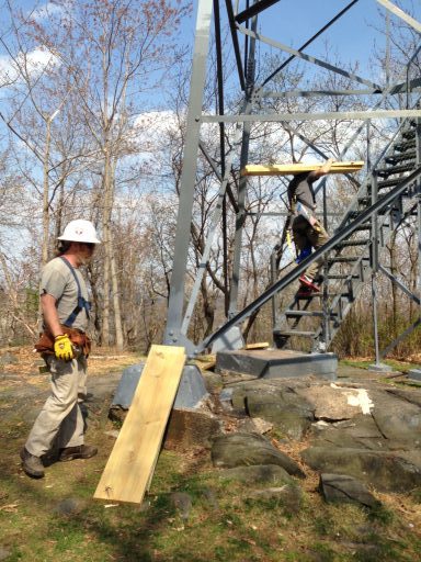 Photo of men carrying lumber for the new floor of the fire tower cabin up the stairs